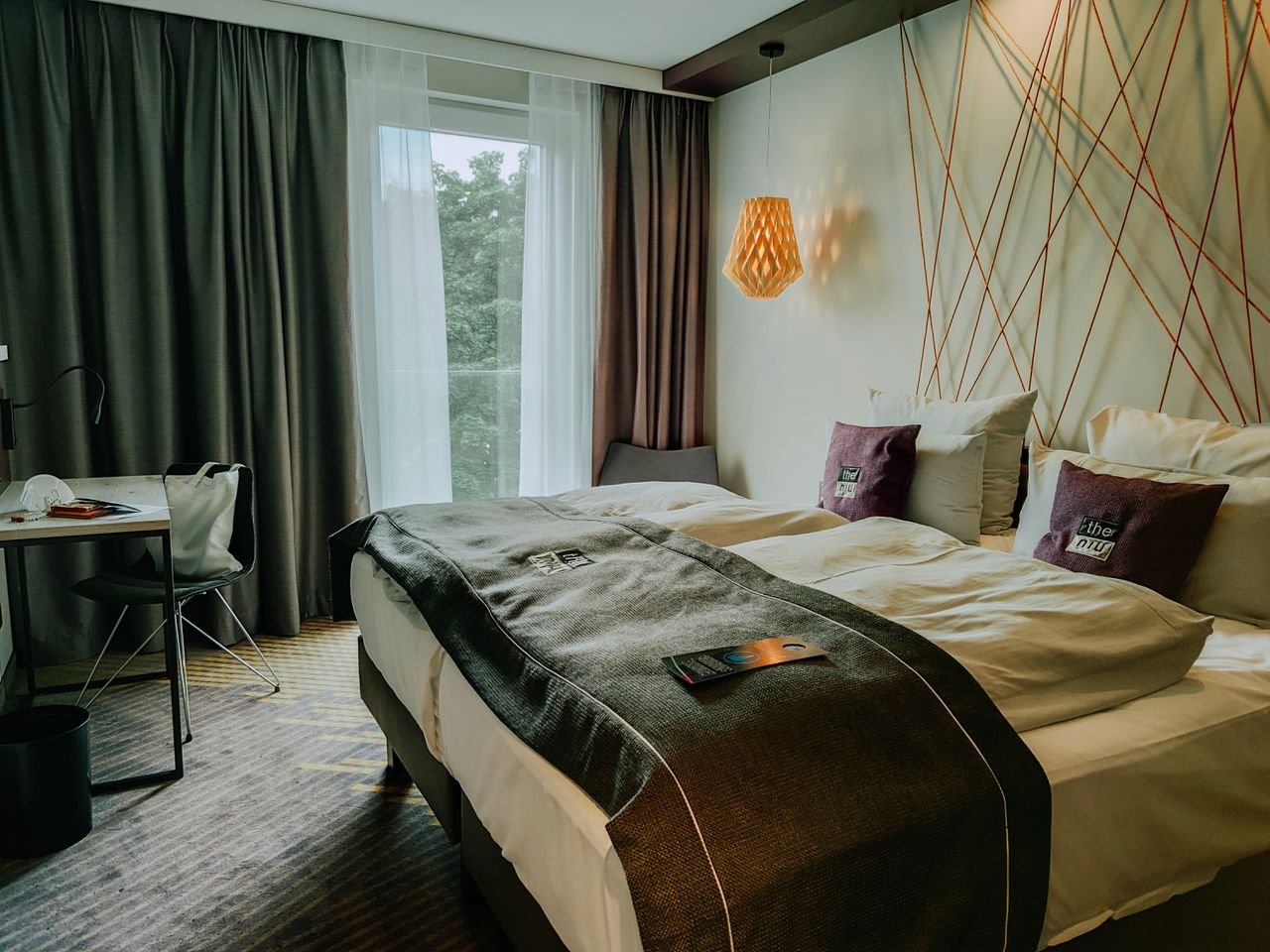 A modern and cozy hotel room featuring a double bed, stylish lighting, and a workspace.